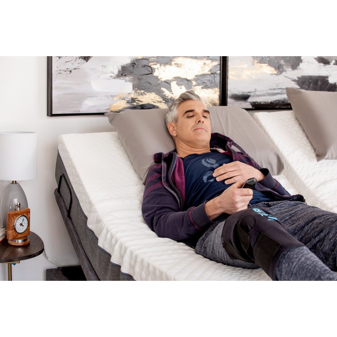 Golden Passport™ Hi Low Adjustable Bed with Dual-Zone Vibrating Massage - with user checking the controls in the remote